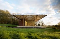 a small structure in the middle of a grassy field with trees and grass around it