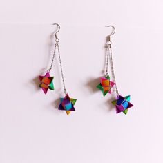 two colorful origami stars hanging from silver chain earring hooks on a white background