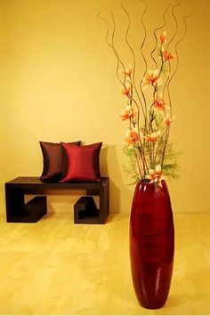 a large vase with flowers in it sitting on the floor next to a small bench