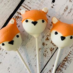 three cake pops with orange frosting and white icing decorated like foxes on them