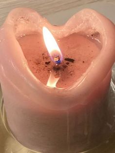 a pink heart shaped candle sitting on top of a metal plate with a lit candle in it