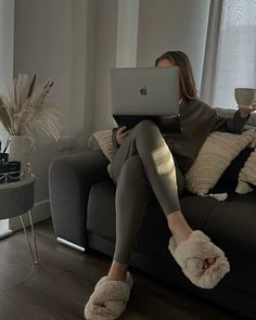 a woman sitting on a couch with her legs crossed and holding a laptop in front of her face