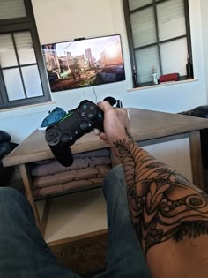 a man holding a video game controller in front of a flat screen tv on top of a wooden table