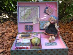 a doll is sitting in a suitcase with other items inside it and on the ground