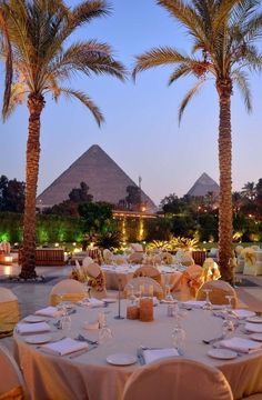 an outdoor dining area with tables, chairs and palm trees in the background at dusk