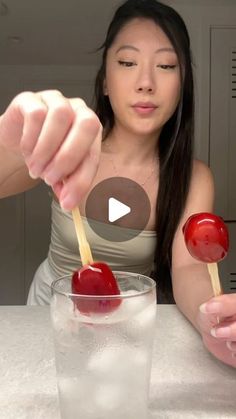 a woman holding two cherries in front of a glass filled with water and ice