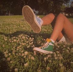 a person sitting in the grass with their feet up and wearing tennis shoes that are green