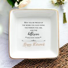 a white and gold plate with a quote on it sitting on a table next to flowers