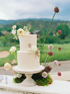 a wedding cake sitting on top of a white table next to flowers and greenery