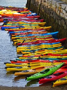 rows of kayaks lined up along the edge of a body of water next to a stone wall