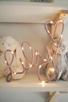 two stuffed animals sitting on top of a white shelf next to lights that spell out the word love