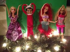 four dolls are posed on top of a christmas tree with lights in front of them