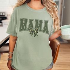 Introducing the Old School Camo Mama Coquette Comfort Colors Sweatshirt, the perfect blend of style and comfort for the modern mom. This camouflage crewneck is not just a fashion statement; it's a cozy companion for a casual day out or lounging at home. Celebrate the spirit of motherhood with our Mama Camo Graphic Sweater, an excellent choice for a Mother's Day gift or a unique Christmas gift for mom. Whether she's wearing it during duck hunting trips or simply enjoying life, this mama camo swea Fall Camouflage T-shirt With Crew Neck, Camouflage Cotton Top With Letter Print, Trendy Camouflage Crew Neck T-shirt, Camouflage Crew Neck Graphic Tee, Camouflage Crew Neck T-shirt With Graphic Print, Camouflage Sublimation Print Crew Neck T-shirt, Camo Sweatshirt, Mom Wardrobe, Graphic Sweaters