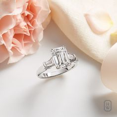 a diamond ring sitting on top of a white surface next to a pink flower and ribbon