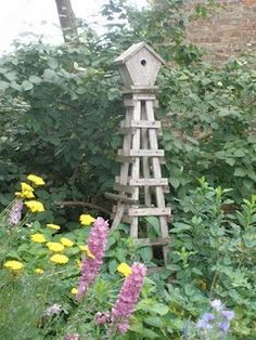 a wooden birdhouse sitting in the middle of a garden filled with wildflowers