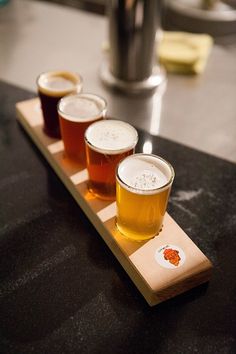 four beers are lined up on a wooden tray