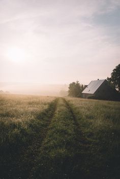 the sun is shining over an open field with a house in the distance and trees to the side