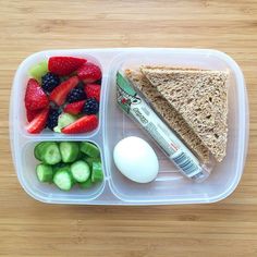 a plastic container filled with fruit and sandwich next to an egg on top of a wooden table