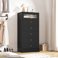 a black chest of drawers next to a white wall with clothes hanging on the rack