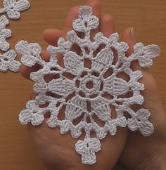 a hand is holding a snowflake made from white crocheted yarns