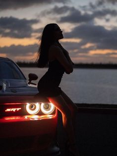 a woman is sitting on the hood of a car at sunset with her legs crossed