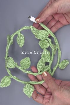 two hands are crocheting leaves on a piece of green yarn that is attached to a string