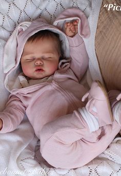 a baby is sleeping on a blanket with its head tucked under a hoodie and it's eyes closed