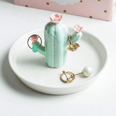 a white plate topped with a green cactus ring holder and two pink flowers on top of it