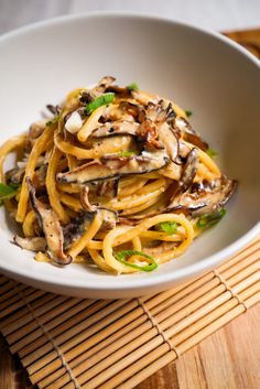 a white bowl filled with pasta covered in mushrooms and sauce on top of a bamboo mat