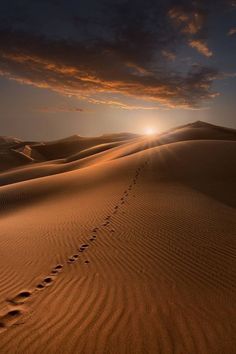 the sun is setting over sand dunes and footprints