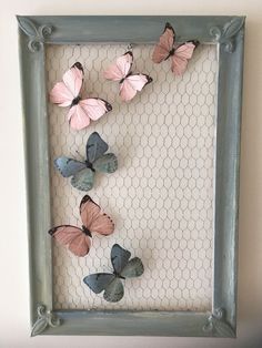 some pink and blue butterflies are in a shadow box with chicken wire on the wall