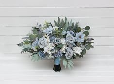 a bouquet of blue flowers and greenery on a white wooden wall with planks