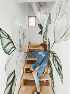 a woman sitting on some steps with flowers painted on the wall above her and behind her