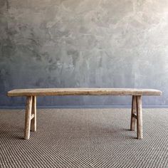 a wooden bench sitting on top of a carpeted floor next to a gray wall