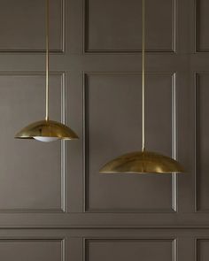 two brass pendant lights hanging from the ceiling in a room with gray walls and wood paneling