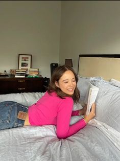 a woman laying on top of a bed holding an open book in her hand and smiling at the camera