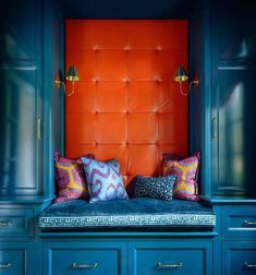 an orange wall behind a blue bench with colorful pillows on it's backrest