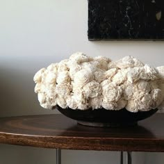 a black bowl filled with white flowers on top of a wooden table next to a painting