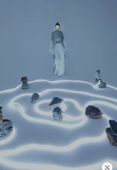 a woman standing in the middle of a white room filled with rocks and stones on top of snow covered ground