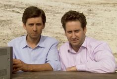 two men sitting next to each other at a table with a laptop computer on it