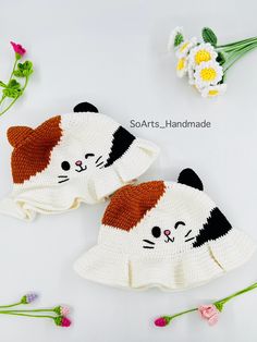 two crocheted hats with cats on them and flowers in the background, one is made out of yarn