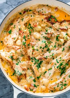 a skillet filled with chicken and sauce on top of a marble countertop next to a wooden spoon