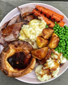 a white plate topped with meat, potatoes and veggies next to carrots