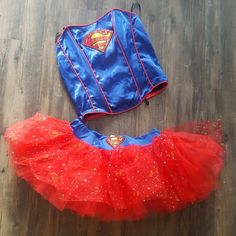 a superman costume is laying on the floor next to a red tutule skirt