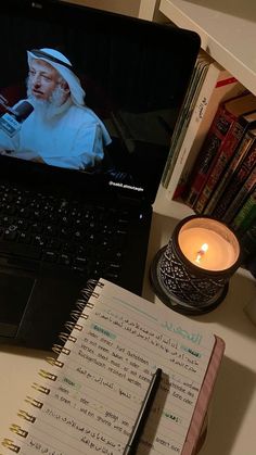 an open laptop computer sitting on top of a desk next to a notebook and candle