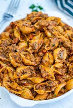 pasta with meat and sauce in a white bowl on a table next to silverware