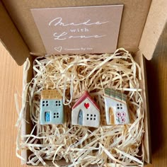 three miniature houses in a cardboard box sitting on a table next to some string wrapped paper