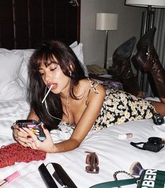 a woman laying on top of a bed holding a cell phone and drinking from a cup