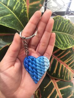 a hand holding a blue heart shaped keychain in front of a green plant