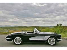 a black and white classic car parked on the side of the road with mountains in the background